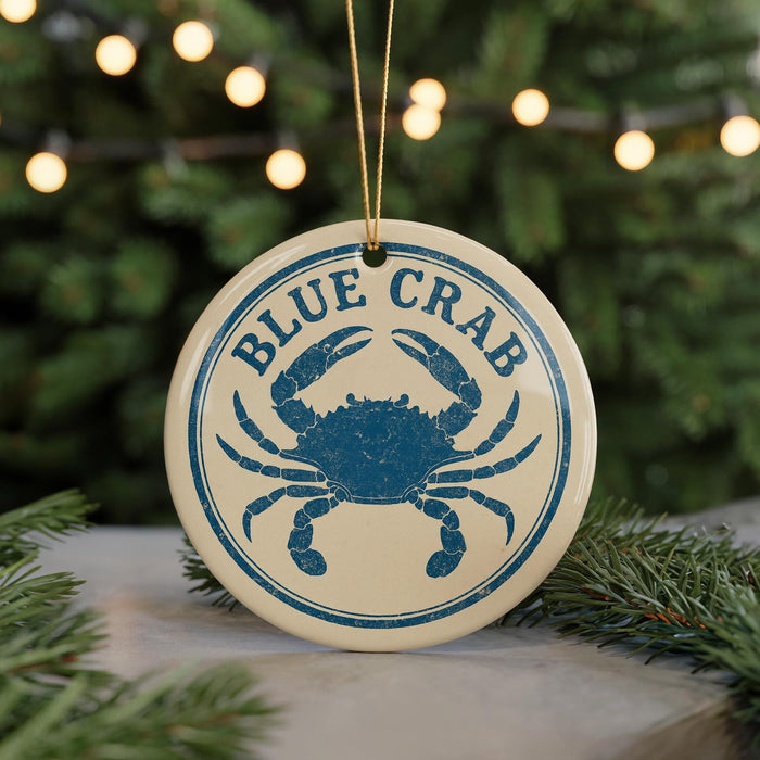 A blue crab ornament with the text "BLUE CRAB" is displayed on a Christmas tree, surrounded by pine branches and twinkling lights.