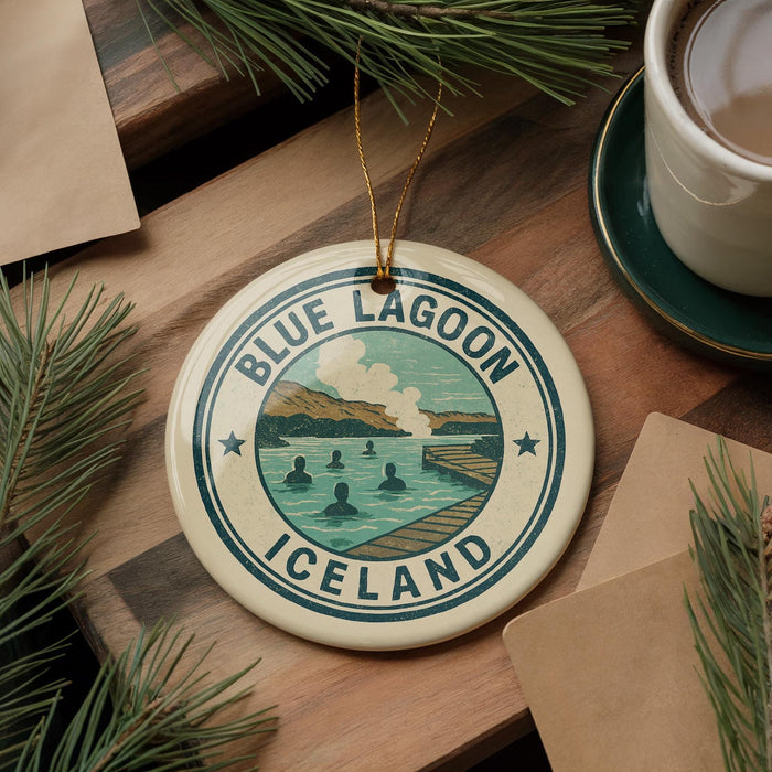 A circular ornament with the text "BLUE LAGOON ICELAND" and an illustration of a lake and mountains, hanging on a branch with pine needles.