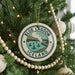 A Christmas tree decorated with ornaments, including a circular ornament with the text "BLUE LAGOON ICELAND" and a scenic illustration of a lake and mountains.