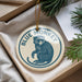 A blue and white ornament with a monkey image, hanging from a string, placed in a box with pine branches.