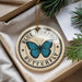 A decorative ornament featuring a blue butterfly, with the text "BLUE MORPHO BUTTERFLY" printed on it, is displayed in a box with pine branches.