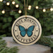 A circular ornament with a blue butterfly design and the text "BLUE MORPHO BUTTERFLY" printed on it, hanging from a string.