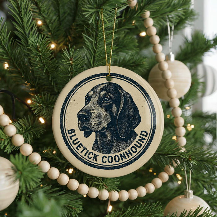 A Christmas tree decorated with ornaments, including a circular ornament with a black and white illustration of a blue and white dog and the text "BLUE TICKET COONHOUND".