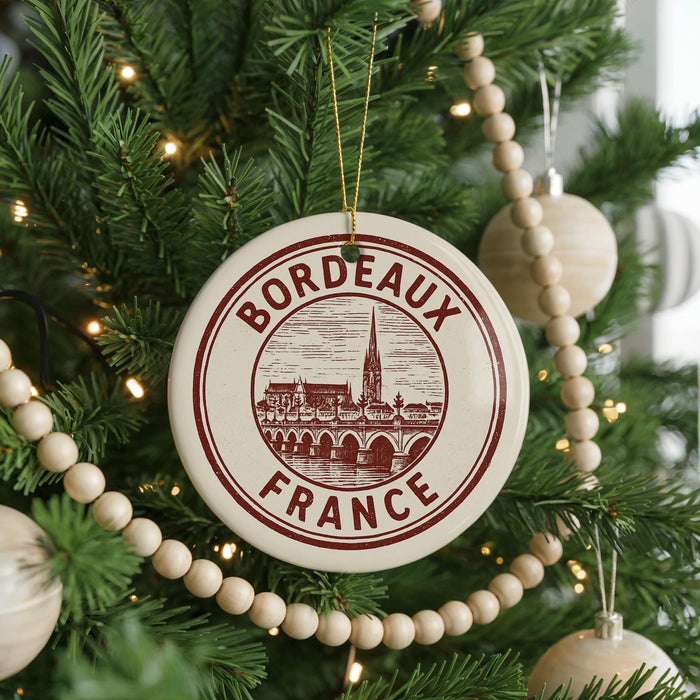 A Christmas tree decorated with ornaments, including a circular ornament with the text "BORDEAUX FRANCE" and a wooden bead decoration.