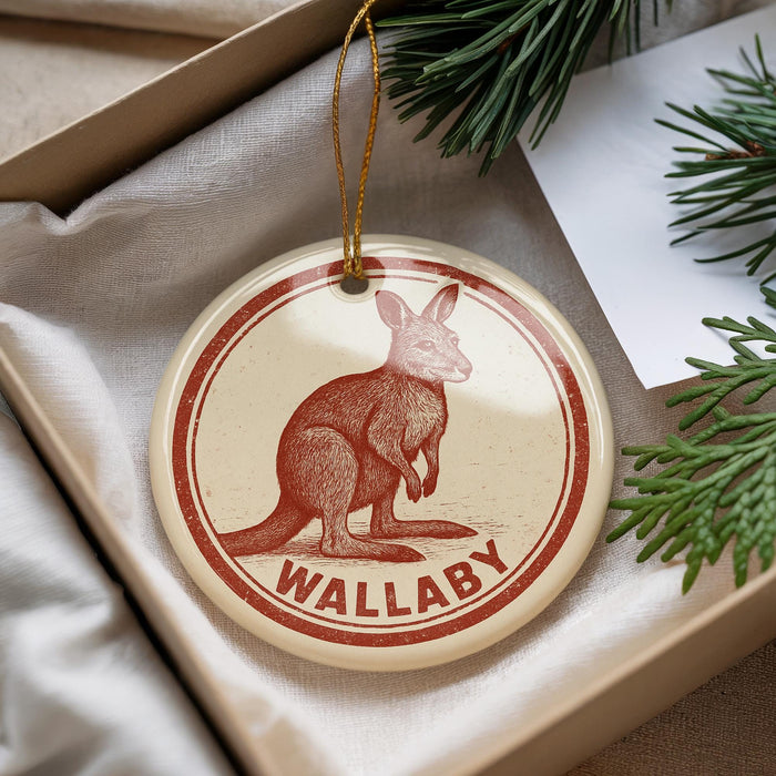 A circular ornament with a kangaroo illustration and the word "Wallaby" printed on it, placed in a box with pine branches.