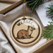A round ornament featuring a weasel, a type of small mammal, is displayed in a box with pine branches.