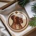 A circular ornament featuring a brown dog's portrait is displayed in a box, surrounded by pine branches.