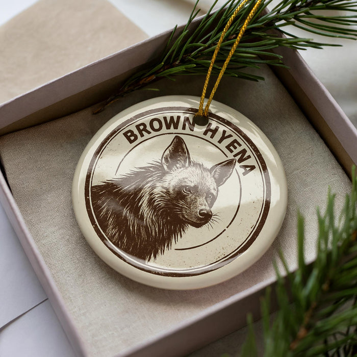 A circular ornament with a brown hyena image and the text "BROWN HYENA" on it, placed in a box with pine branches.