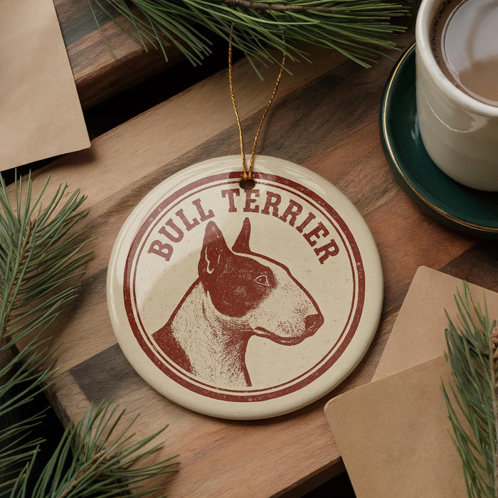 A bull terrier ornament is displayed on a wooden surface, surrounded by pine branches and a cup of coffee.