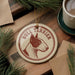 A bull terrier ornament is displayed on a wooden surface, surrounded by pine branches and a cup of coffee.
