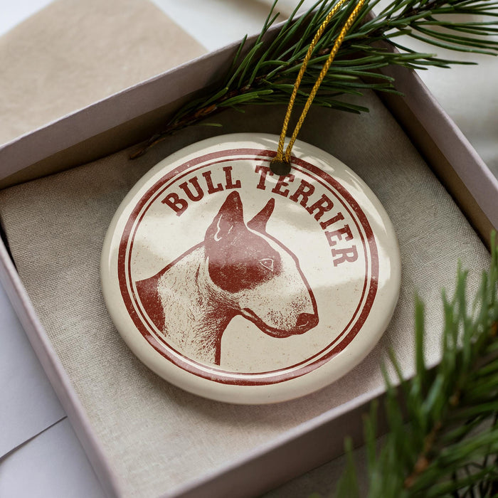 A circular ornament with a bull terrier image and the word "Bull Terrier" written on it, placed inside a box with pine branches.