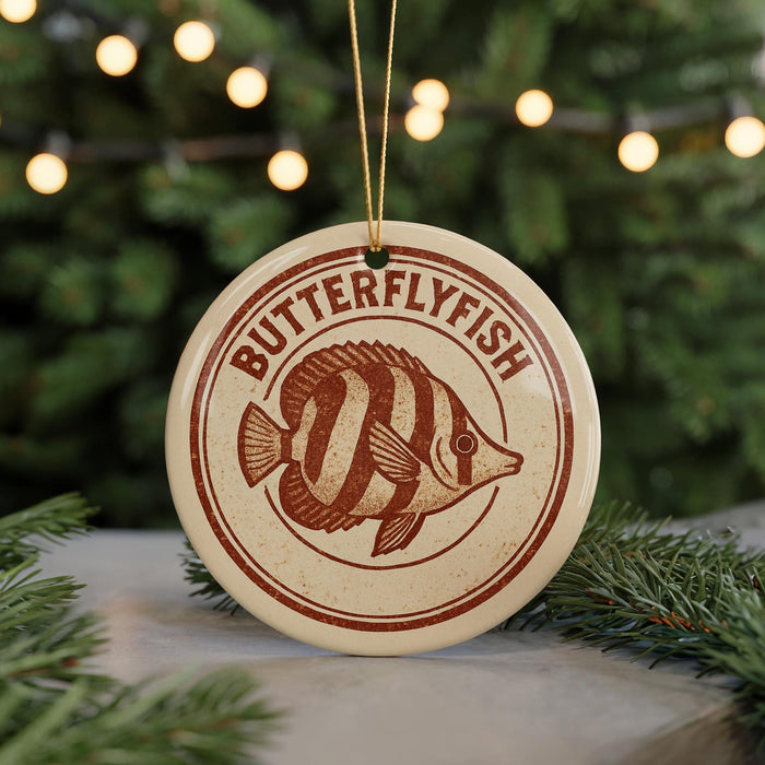 A circular ornament with the text "BUTTERFLY FISH" and an illustration of a butterflyfish is displayed on a table, with a blurred background of a Christmas tree.
