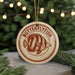 A circular ornament with the text "BUTTERFLY FISH" and an illustration of a butterflyfish is displayed on a table, with a blurred background of a Christmas tree.