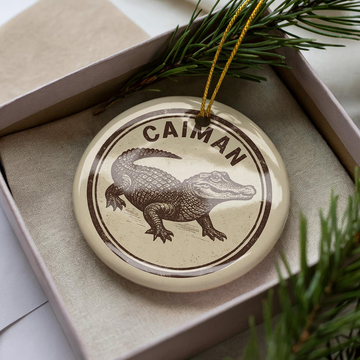 A circular ornament with a brown and white illustration of a crocodile, and the word "CAIMAN" written around the edge.