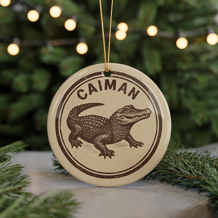 A circular ornament featuring a cartoon alligator, with the word "CAIMAN" written around the top edge.