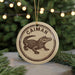 A circular ornament featuring a cartoon alligator, with the word "CAIMAN" written around the top edge.