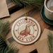 A round ornament with the text "CALIFORNIA SEA LION" and a seal illustration is displayed on a wooden surface, surrounded by pine branches and a cup of coffee.