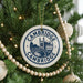 A Christmas tree decorated with ornaments, including a circular ornament with the text "Cambridge" and a castle illustration, surrounded by lights and greenery.