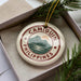 A decorative ornament in a box, featuring the text "CAMIGUIN PHILIPPINES" and a mountain landscape design.