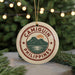 A round ornament with the text "CAMIGUIN PHILIPPINES" and a graphic of a mountain and water, hanging from a string against a background of Christmas lights and greenery.