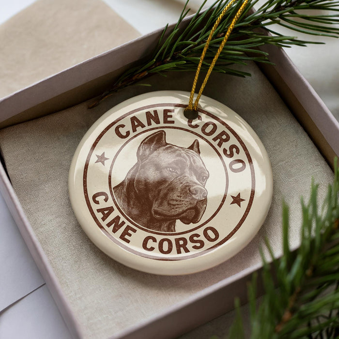A ceramic ornament in a box, featuring a brown and white image of a dog's head and the text "CANE CORSO" around the edge.