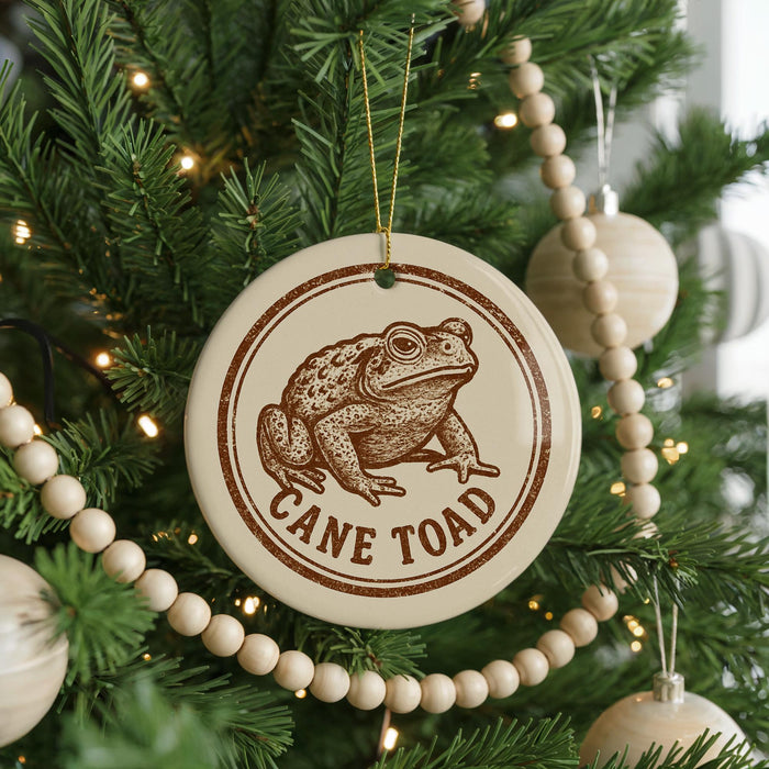 A Christmas tree decorated with ornaments, including a round ornament with a frog image and the text "CANE TOAD" printed on it.