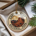 A decorative ornament with the text "CAPITOL REEF NATIONAL PARK" on it, featuring an illustration of a desert landscape with mountains and a sun.