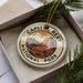 A decorative ornament in a box, featuring a circular design with a mountain landscape and the text "CAPITOL REEF NATIONAL PARK".