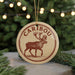 A circular ornament with a deer illustration and the word "CARIBOU" written on it, hanging from a string.