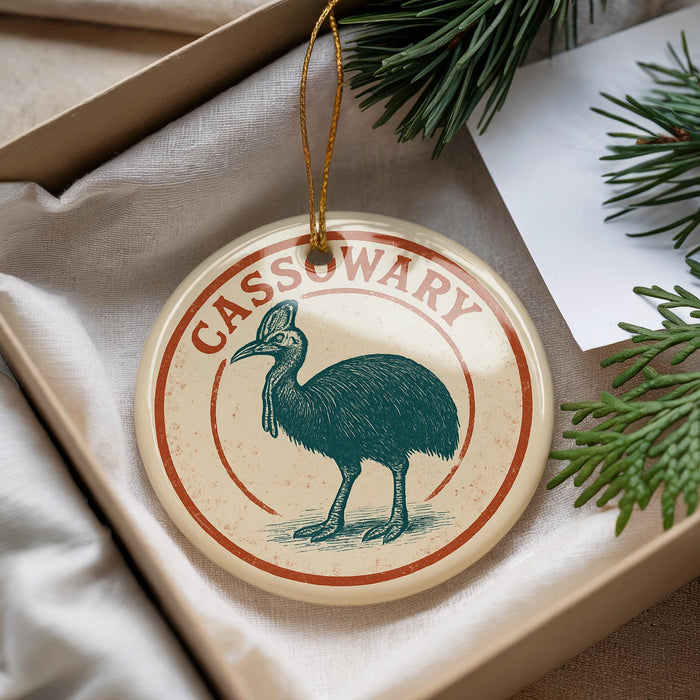 A circular ornament with a bird illustration and the word "CASSOWARY" written on it, placed in a box with pine branches.