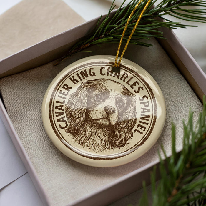 A ceramic ornament in a box, featuring a portrait of a Cavalier King Charles Spaniel dog.