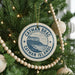A circular ornament on a Christmas tree, featuring the text " Cayman Islands" and a graphic of a tropical island landscape.