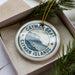 A circular ornament with the text " Cayman Islands" printed on it, surrounded by pine branches.