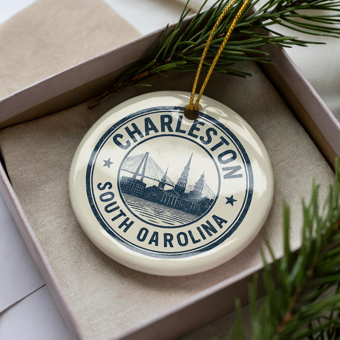 A decorative ornament in a box, featuring a circular design with the text "CHARLESTON SOUTH CAROLINA" and an illustration of a bridge.
