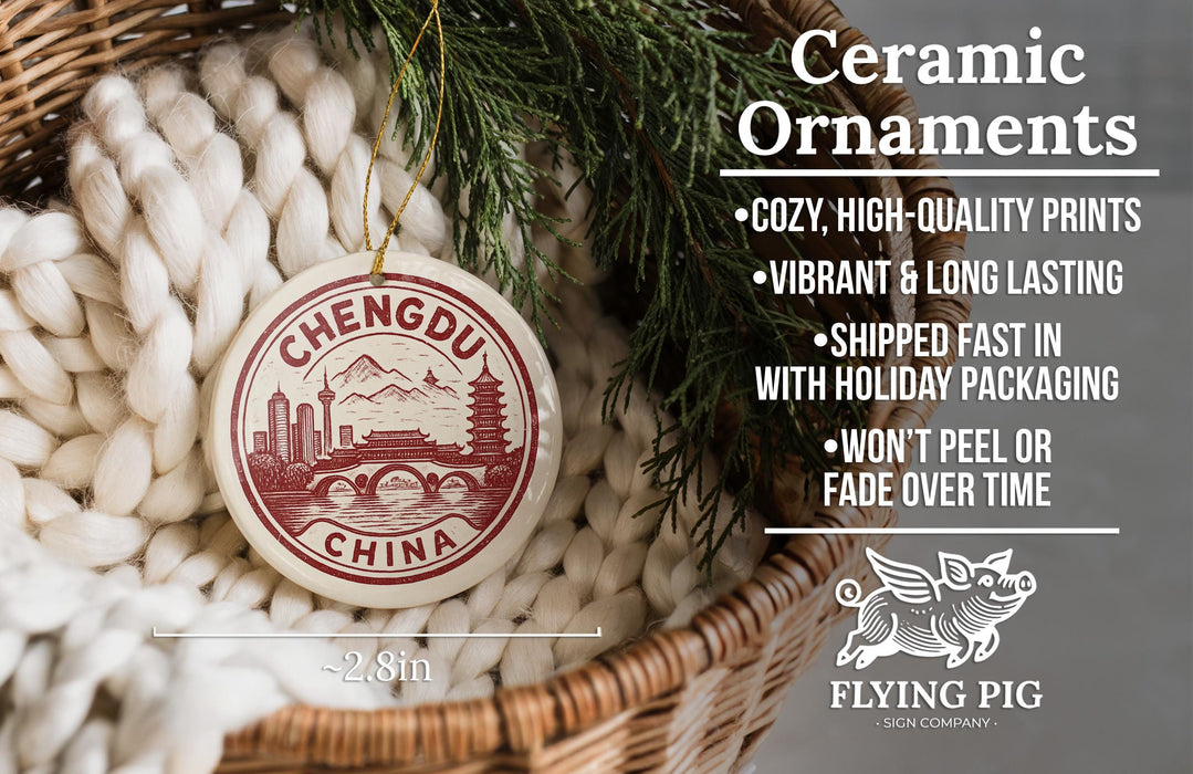 Ceramic ornaments, specifically a round ornament with a cityscape design, are displayed in a basket with greenery.