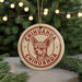 A round ornament with a chihuahua dog's face printed on it, surrounded by Christmas lights and greenery.