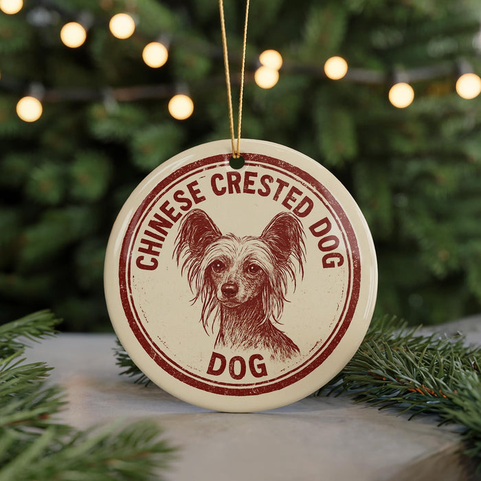 A round ornament with a red and white design featuring a dog's face and the text "CHINESE CREsted DOG DOG" is displayed in front of a blurred Christmas tree.