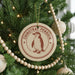 A round ornament with a penguin design hangs on a Christmas tree, surrounded by other ornaments and lights.
