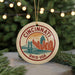 A circular ornament with a graphic of a city skyline and the text "CINCINNATI, OHIO, USA" on it, hanging from a string.