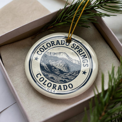A decorative ornament in a box, featuring a mountain landscape and the text "COLORADO SPRINGS COLORADO USA".