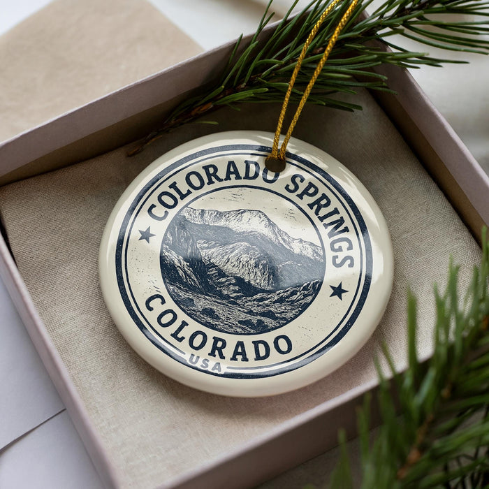 A decorative ornament in a box, featuring a mountain landscape and the text "COLORADO SPRINGS COLORADO USA".