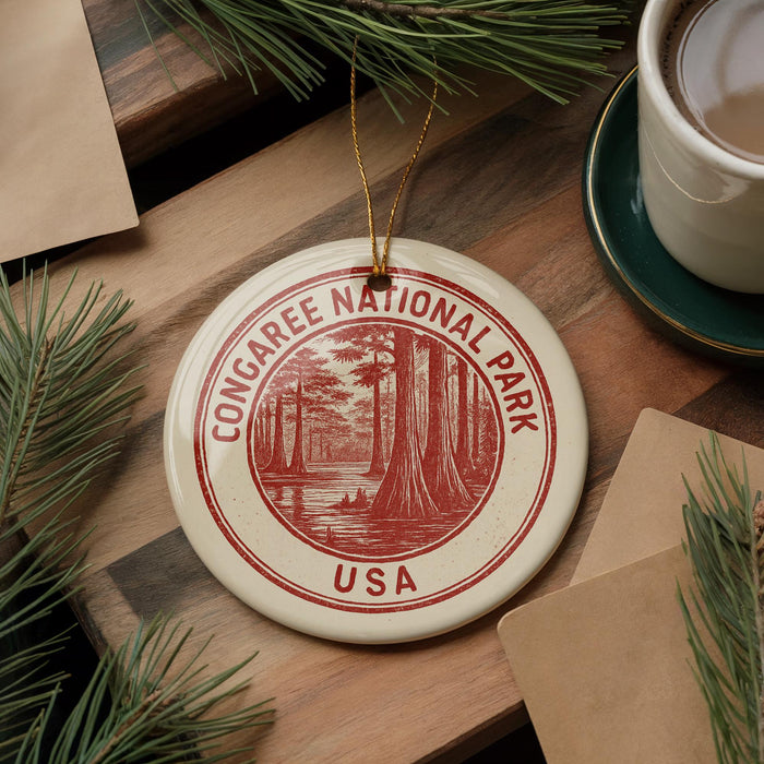 A circular ornament with the text "CONGAREE NATIONAL PARK USA" printed on it, surrounded by pine branches and a cup of coffee on a wooden surface.