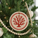 A Christmas tree decorated with ornaments, including a round ornament with a red tree design and a string of wooden beads.
