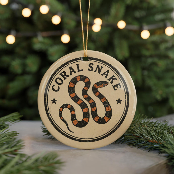 A round ornament with the text "CORAL SNAKER" and a graphic of a snake is displayed in front of a Christmas tree with twinkling lights.
