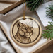A round ornament featuring a close-up of a cougar's face, with a pine branch and a white card visible in the background.