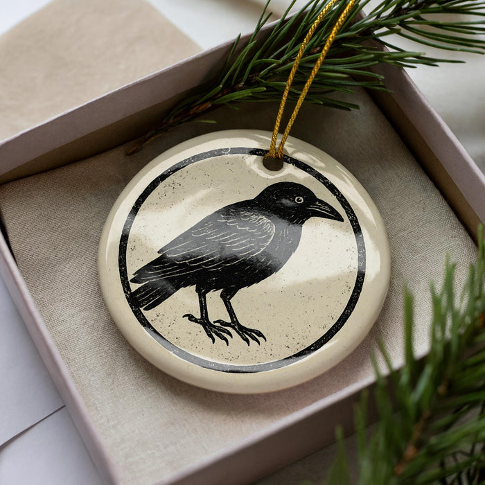 A ceramic ornament in the shape of a black bird is displayed in a box, surrounded by pine branches.