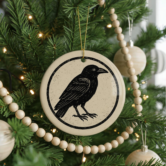 A ceramic ornament featuring a black bird is hanging on a Christmas tree, surrounded by a string of beads and other ornaments.