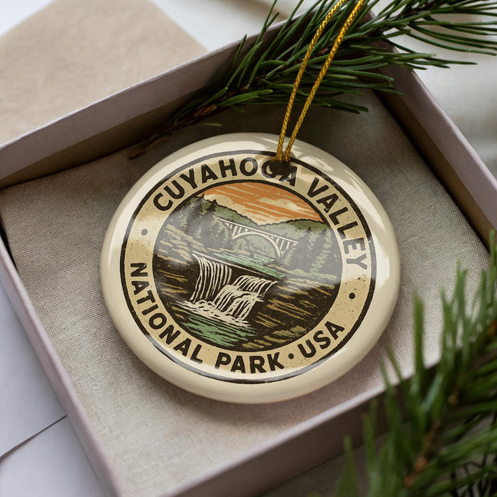 A decorative ornament with the text "CUYAHOGA VALLEY NATIONAL PARK USA" on it, placed in a box with pine branches.