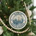 A Christmas tree decorated with ornaments, including a circular ornament with a cityscape and text, surrounded by lights and greenery.