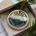 A decorative ornament in a box, featuring a mountain landscape and the text "DENALI NATIONAL PARK USA".